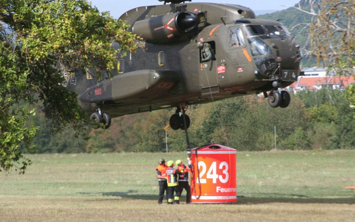 Ein Hubschrauber mit Löschtank schwebt knapp über dem Boden Ein Hubschrauber mit Löschtank schwebt knapp über dem Boden